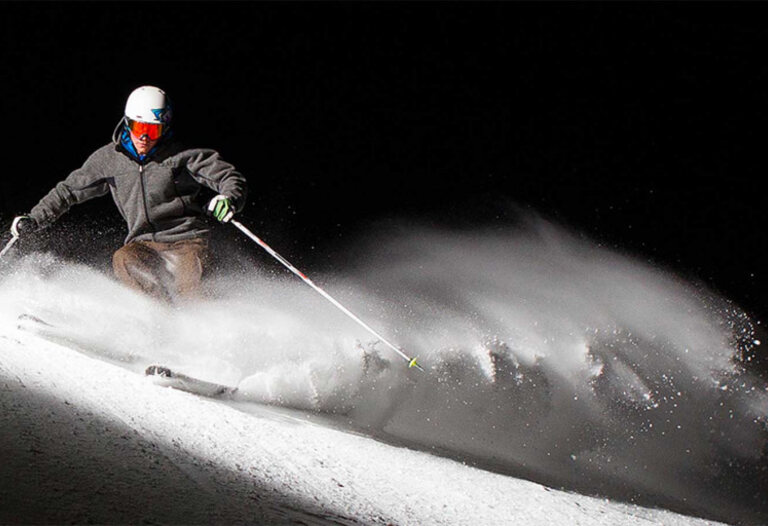Sciatore sulla pista illuminata di notte in Paganella